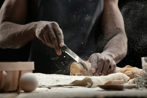 Close up of african-american man slices fresh bread with a kitchen knife