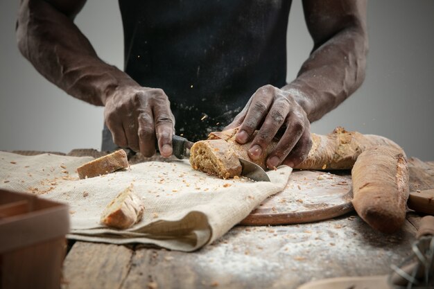 アフリカ系アメリカ人の男のクローズアップは、包丁で焼きたてのパンをスライスします