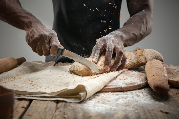Close up of african-american man slices fresh bread with a kitchen knife
