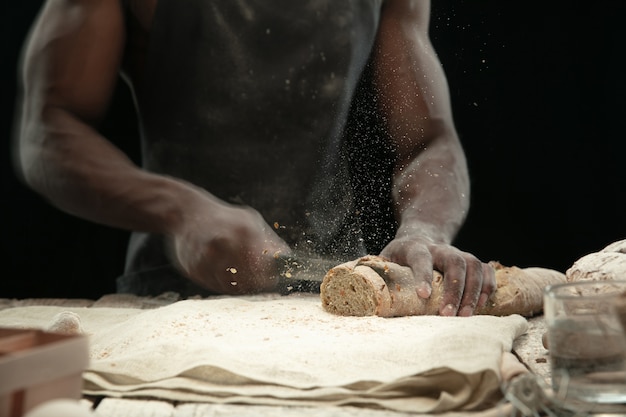 アフリカ系アメリカ人の男のクローズアップは、包丁で焼きたてのパンをスライスします