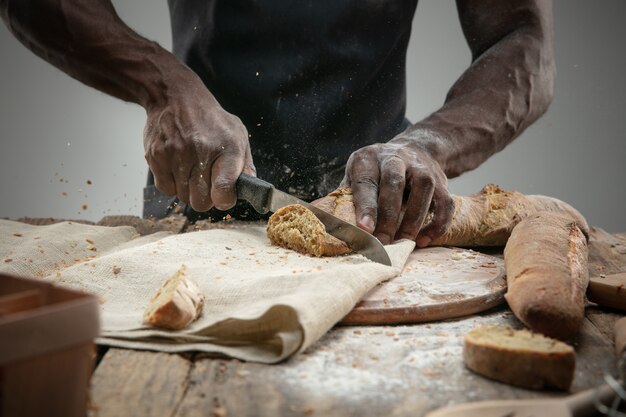 アフリカ系アメリカ人の男のクローズアップは包丁で焼きたてのパンをスライスします