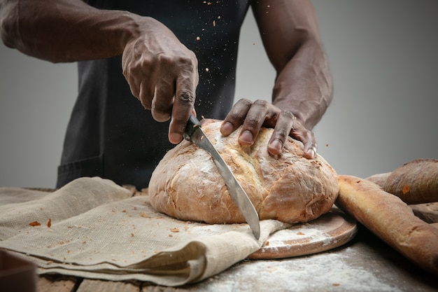 Close up of african-american man slices fresh bread with a kitchen knife