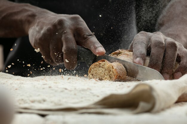 Close up of african-american man slices fresh bread with a kitchen knife