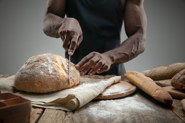 Free photo close up of african-american man slices fresh bread with a kitchen knife