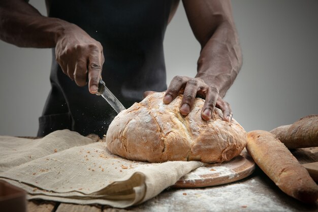 Close up of african-american man slices fresh bread with a kitchen knife