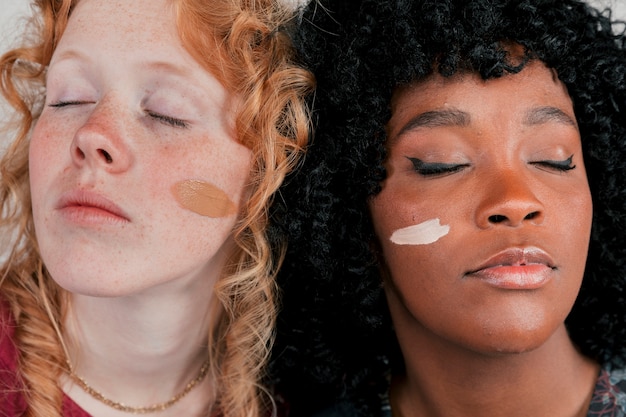 Крупный план лица африканских и кавказских женщин с кремом тона кожи на щеке
