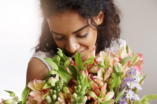 Free photo close up of african woman florist smiling holding sniffing bouquet of alstroemerias. closed eyes.