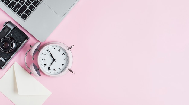 Close-up of alarm clock; camera; envelope and laptop against pink background