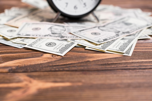 Close-up of alarm clock over the us dollar currency notes on wooden desk