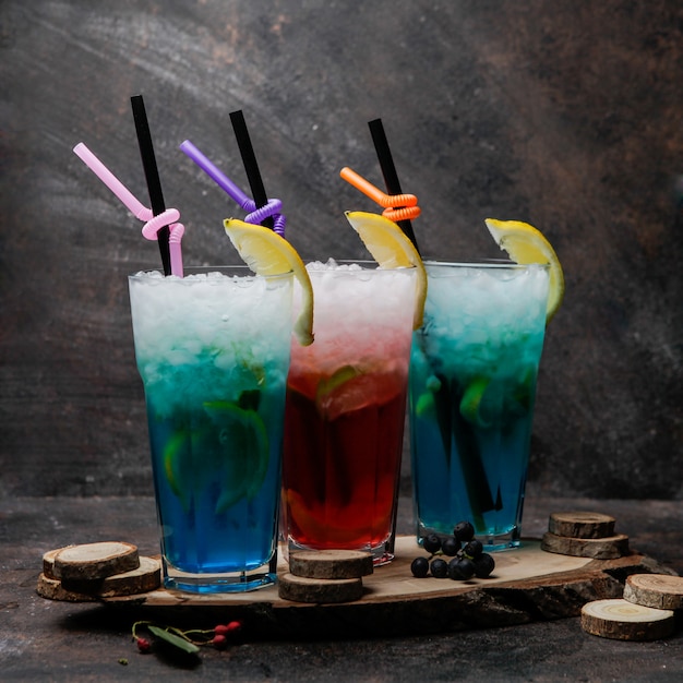 Алкогольные коктейли крупным планом, бокалы из голубой лагуны, коктейль с лимоном и бокал с виски на деревянной подставке