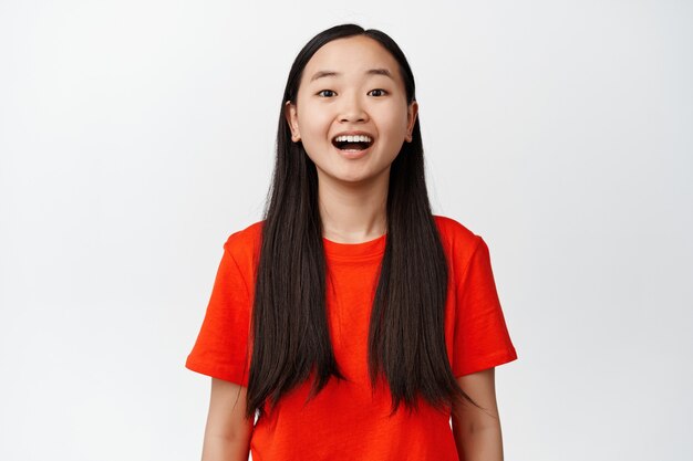 Close up of amazed brunette asian girl, drop jaw and gazing with fascination and joy on white, looking at something cool on white