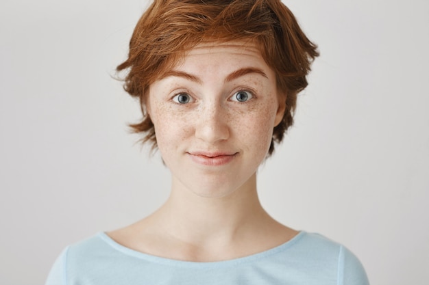 Close-up of amused and surprised redhead girl posing against the white wall