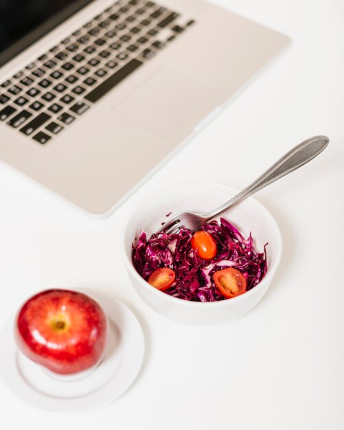 Close-up of apple and laptop near red cabbage and tomatoes in bowl