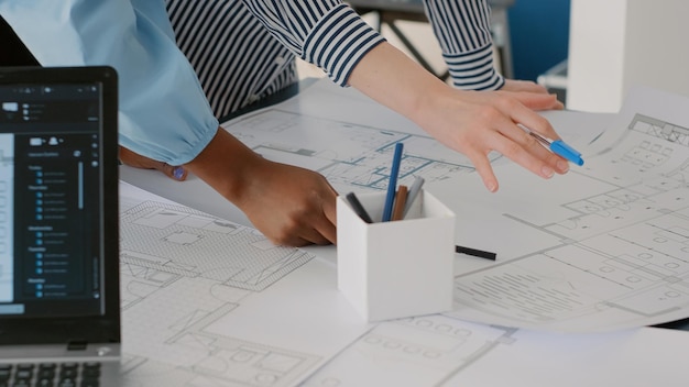 Закройте архитекторов, работающих в команде, чтобы разработать планы чертежей для построения модели на столе. Группа женщин, работающих с промышленным эскизом и планом печати макета. Архитектурный проект