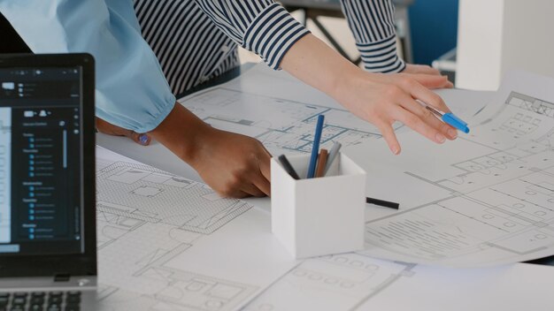 Закройте архитекторов, работающих в команде, чтобы разработать планы чертежей для построения модели на столе. Группа женщин, работающих с промышленным эскизом и планом печати макета. Архитектурный проект