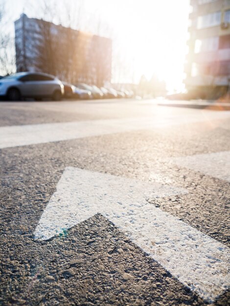 Close-up of arrow on asphalt with view of the street