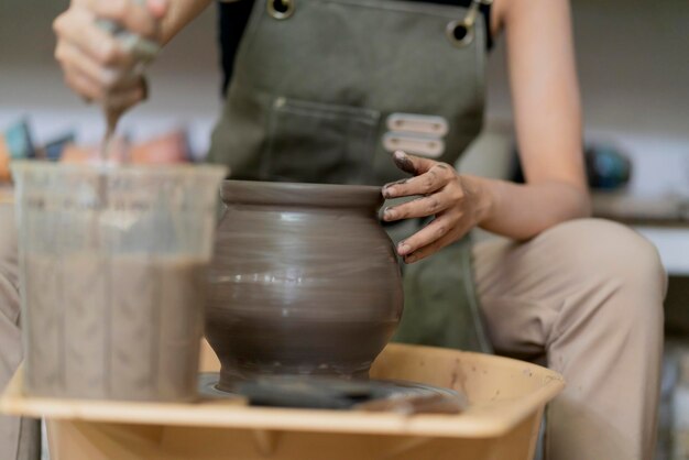 Close up of asian artist ceramist female hands working on potters wheelasian female sculpture woman with wet dirty hands shaping clay vase on pottery wheel at workshop studio