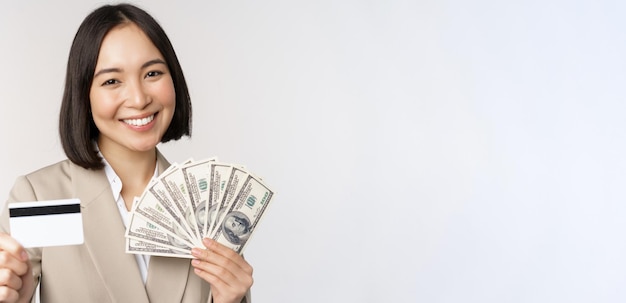 흰색 배경 위에 정장을 입고 서 있는 신용 카드와 돈을 보여주는 아시아 여성 사업가의 클로즈업