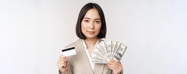 흰색 배경 위에 정장을 입고 서 있는 신용 카드와 돈을 보여주는 아시아 여성 사업가의 클로즈업
