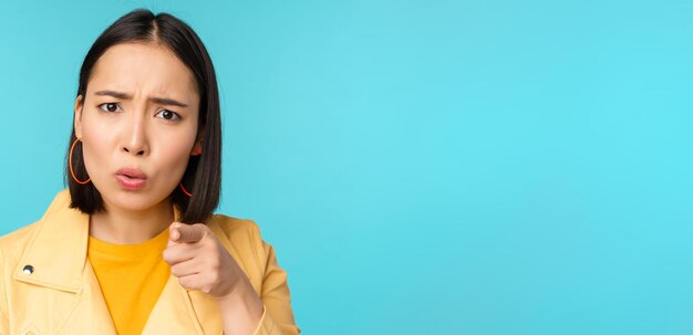 Close up of asian girl accusing and pointing finger at camera looking offended or displeased scoldin