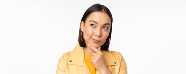 Close up of asian woman thinking looking up thoughtful pondering smth with pleased smiling face stan