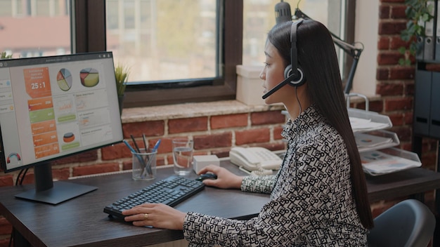 Close up of asian woman with headphones talking on phone call to people at customer service. Consultant using headset and microphone, working at call center on computer. Support chat