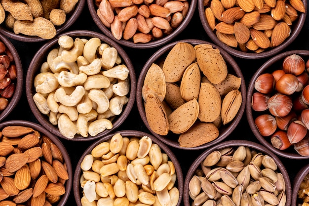 Close-up assorted nuts and dried fruits in mini different bowls with pecan, pistachios, almond, peanut, cashew, pine nuts