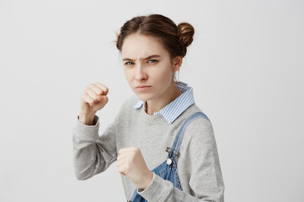 Close up attack position of confident woman being ready to fight looking on her offender. Frowning schoolgirl going to punch with strength training at sport club. Behaviour, sport