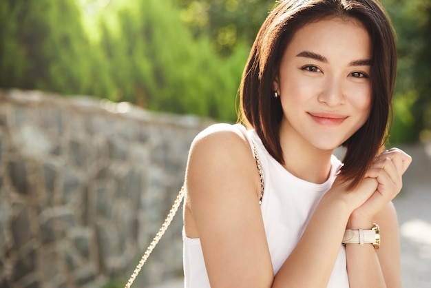 Close-up attractive asian woman smiling at camera, walking in park