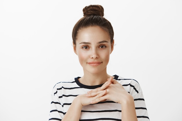 Free photo close-up of attractive brunette girl with hairbun, clasp hands together and smiling, concept of beauty and fashion