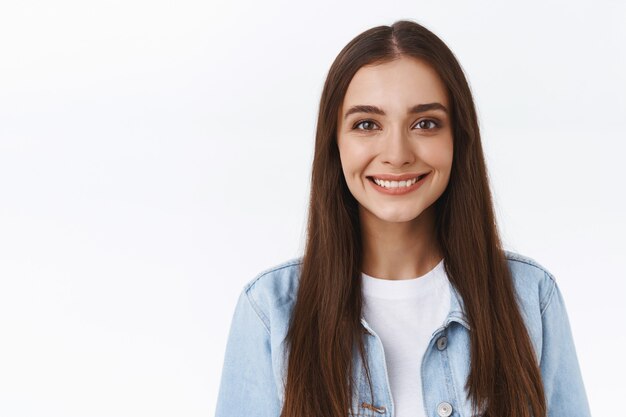 Close-up attractive tender and feminine young woman with long hairstyle, smiling silly and cute with casual relaxed expression, standing over white background in denim jacket, show positive emotion