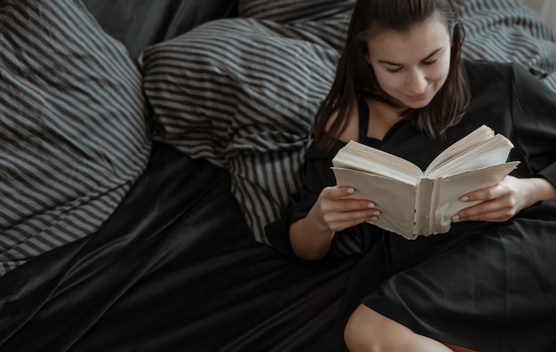 Close up of an attractive woman reading a book while lying in a cozy bed.