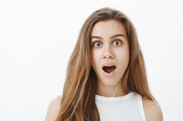 Close-up of attractive young woman looking surprised, drop jaw, say wow in amazement