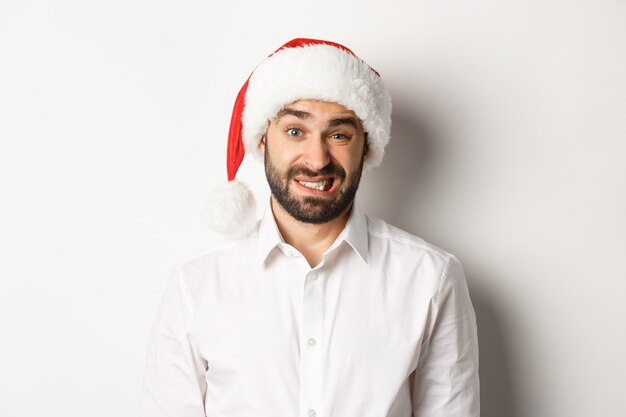 Close-up of awkward guy in santa hat apologizing, feeling uncomfortable, standing   Christmas concept.