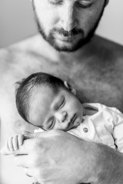 お父さんの腕の中で眠っているクローズアップの赤ちゃん