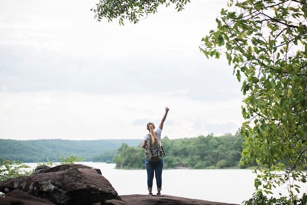 Close up back of tourist girl with arms raising happy with nature near lake. Travel concept.