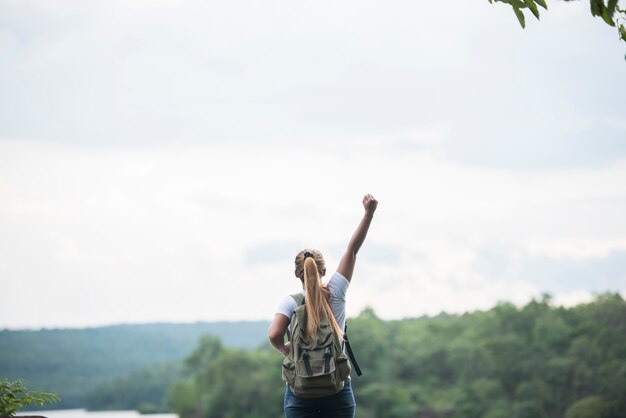 Close up back of tourist girl with arms raising happy with nature near lake. Travel concept.