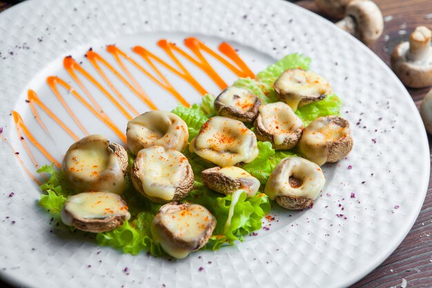 Close up baked mushrooms with cheese and lettuce on a white plate