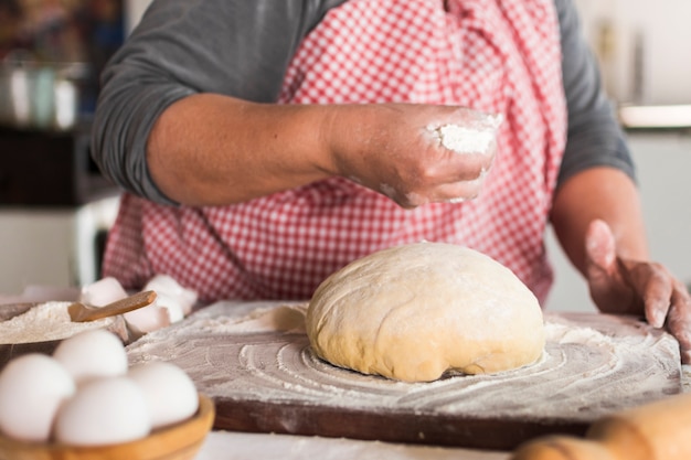 Free photo close-up of baker dusting flour on the knead dough over the wooden table