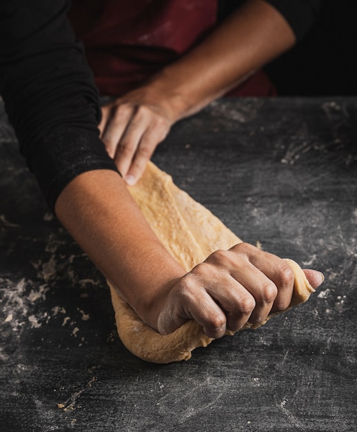 Close-up baker hands kneading on top dough composition