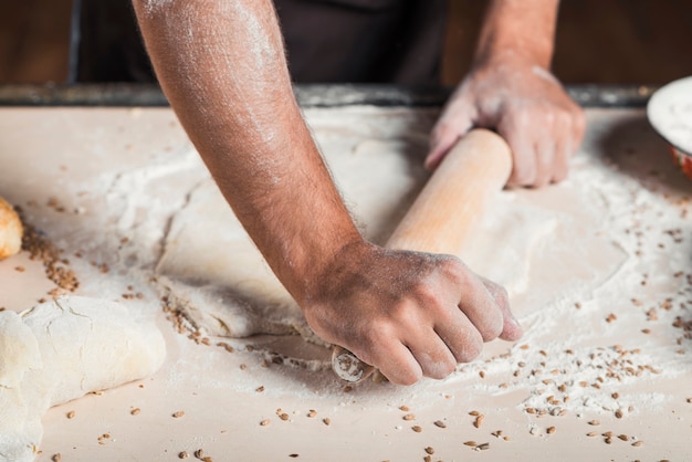 Close-up of baker's hand flattening dough on kitchen counter