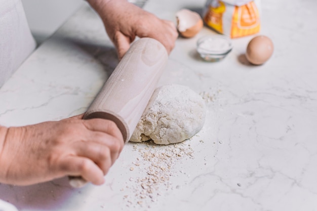 Close-up of a baker's hand flattening dough with rolling pin