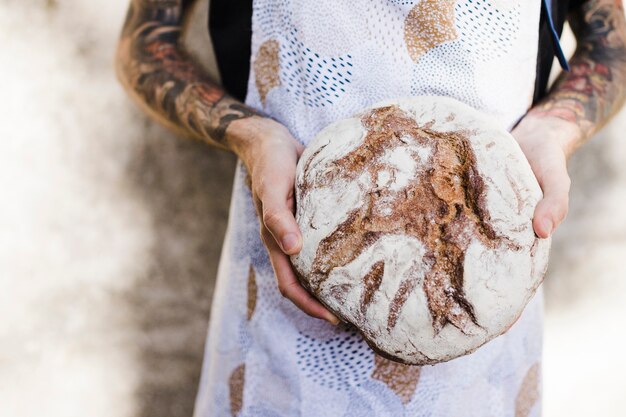 丸い素朴なパンを持っているパン屋の手のクローズアップ
