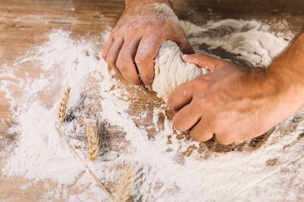 Close-up of baker's hand kneading dough on wooden table