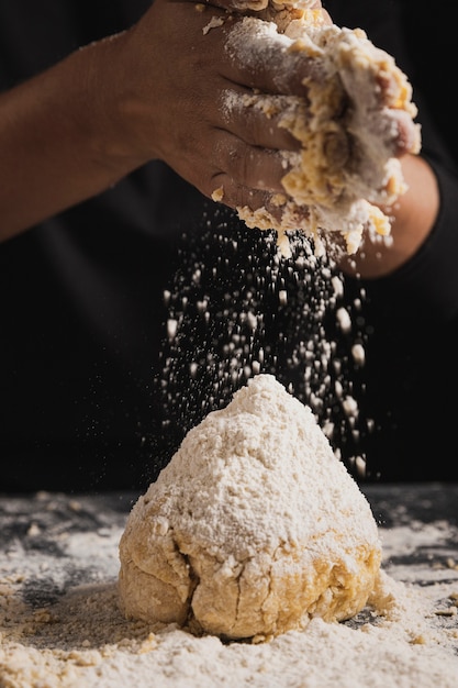 Close-up baker spreading flour on dough