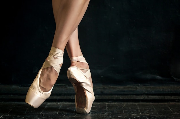 Free photo close-up ballerina's legs in pointes on black wooden floor