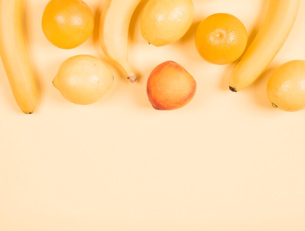 Close-up of banana; lemon; orange and peach on beige background