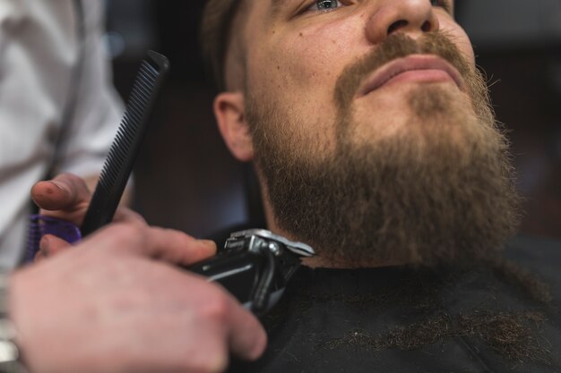 Close-up barber trimming beard of man