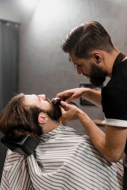 Крупный план парикмахерской обрезка мужской бороды с электрическим триммером