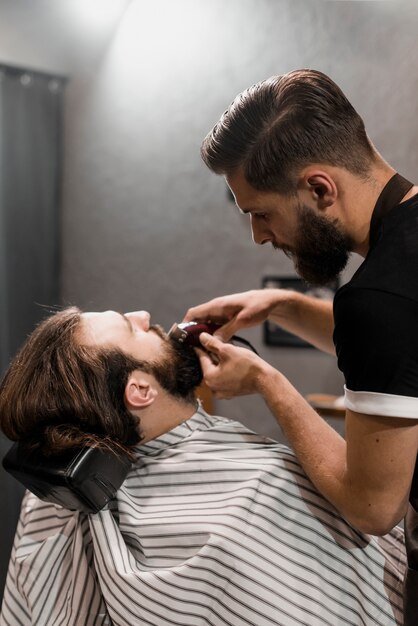 Close-up of a barber trimming man's beard with electric trimmer